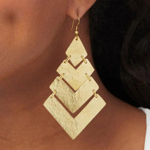 A close-up of an ear dawning a gold earring in a shepherd hook design.