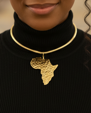 Woman wearing a black turtleneck and gold necklace with an African design in a blurred indoor setting