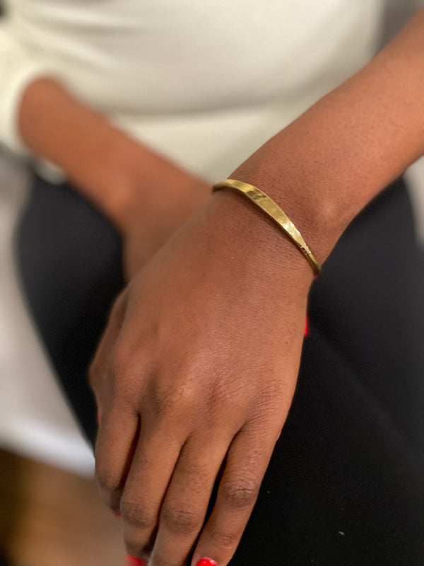 A woman's closeup of their wrist wearing a golden brass bangle.