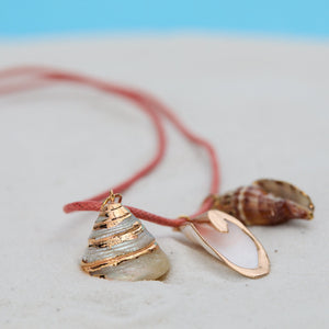 Necklace with shell pendant and pink cord on sand with blue background