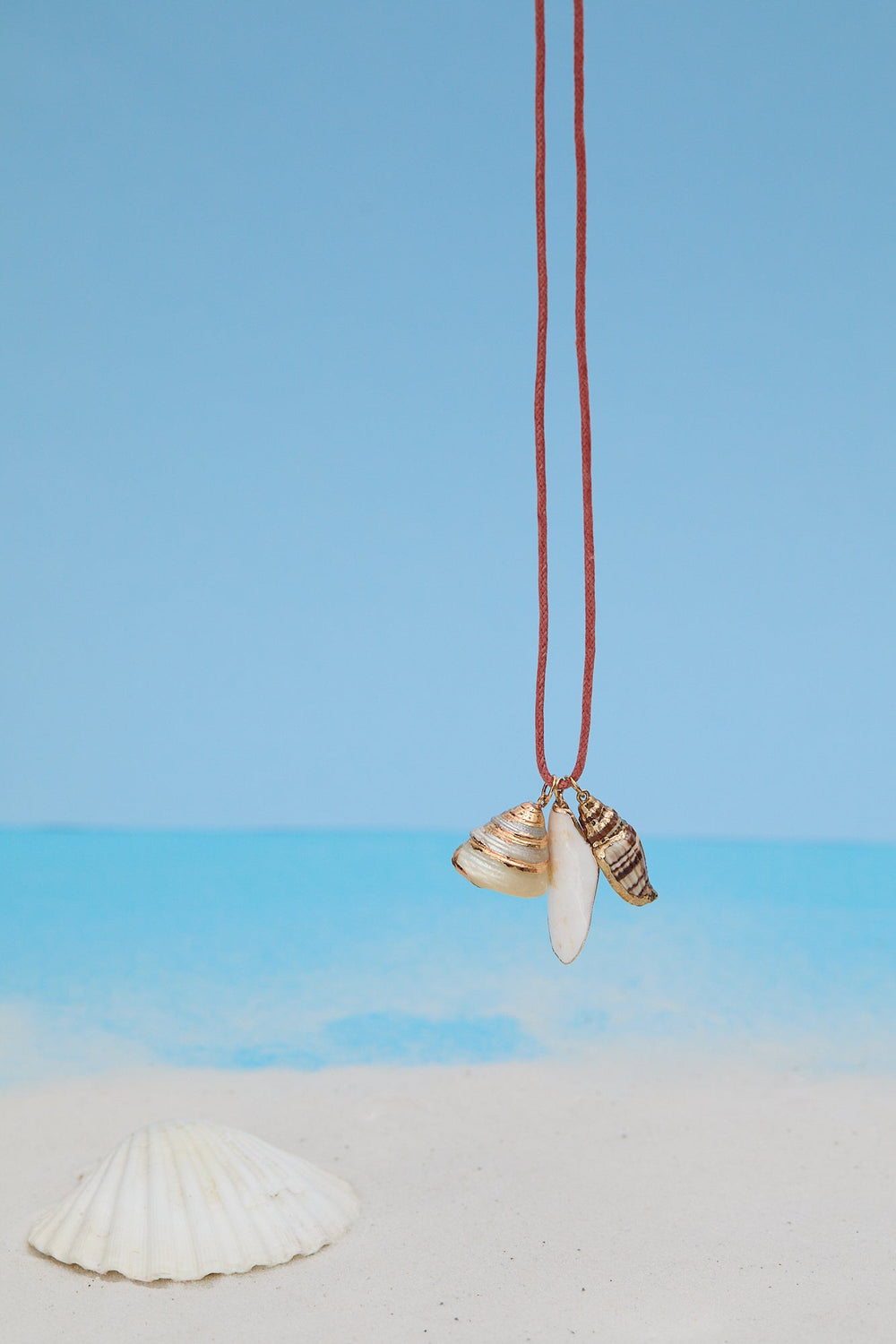 Necklace with shell pendant and pink cord on sand with blue background