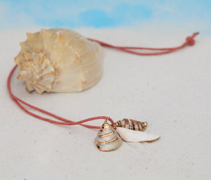 Necklace with shell pendants on a sandy surface next to a seashell