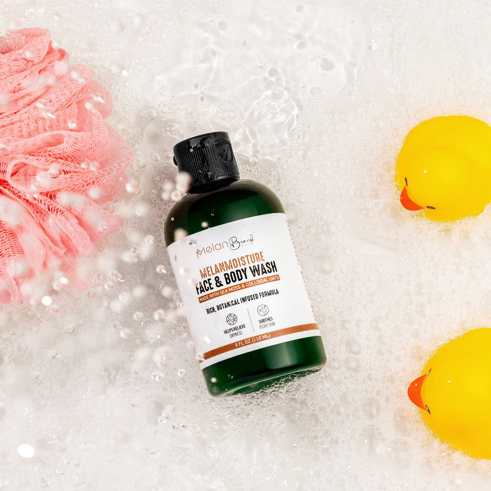 Bottle of Melano Moisture Face & Body Wash surrounded by bath items on a soapy background