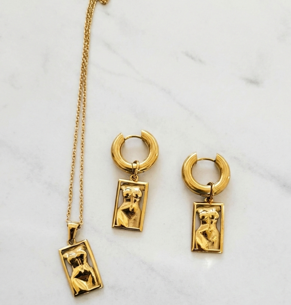 Gold necklace and hoop earrings with pendant on a marble surface