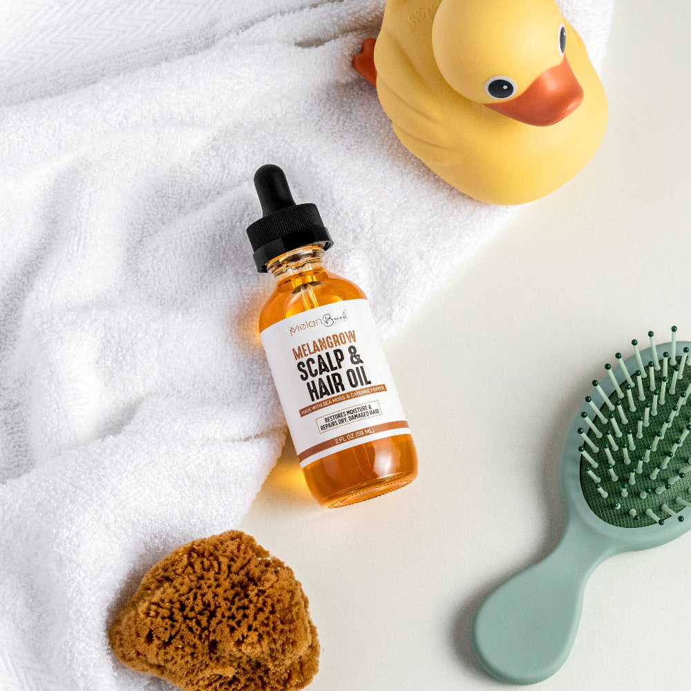 Bottle of scalp and hair oil with a brush, sponge, and rubber duck on a towel