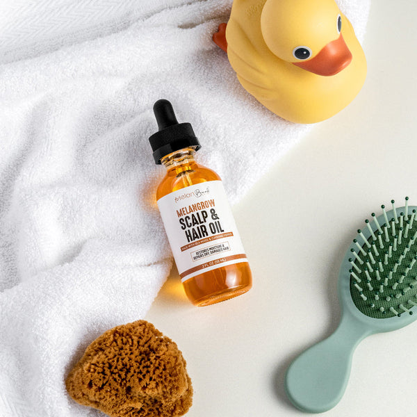 Bottle of scalp and hair oil with a brush, sponge, and rubber duck on a towel