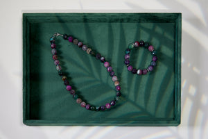 Gemstone necklace and bracelet set on a green tray with leaf shadows
