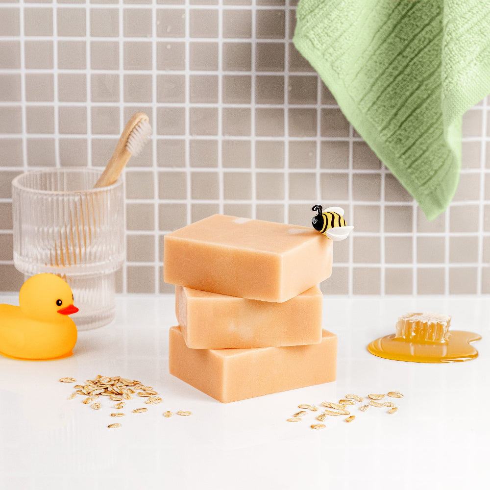 Stack of Oat meal Milk Honey Soap bars on a bathroom counter with a rubber duck and towel in the background.