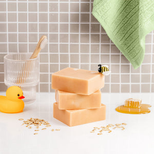 Stack of Oat meal Milk Honey Soap bars on a bathroom counter with a rubber duck and towel in the background.