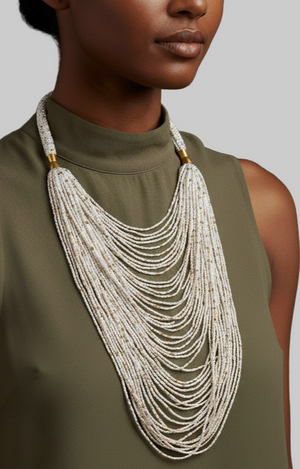 Woman wearing a green sleeveless top with a long, layered necklace against a gray background