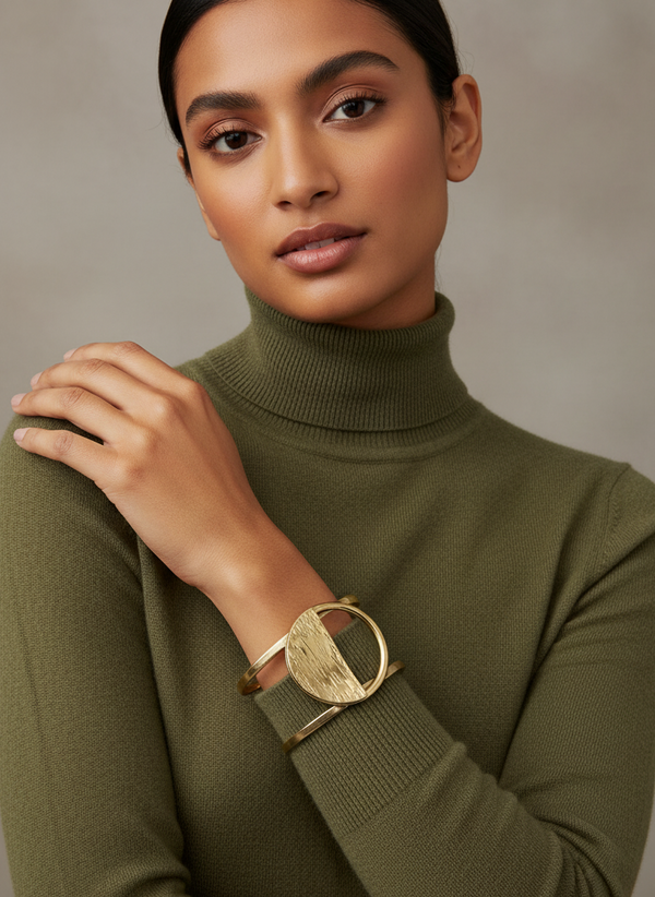 Woman wearing a green turtleneck sweater with a gold bracelet on a neutral background