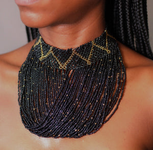 A close-up image of a person wearing a black beaded choker necklace with a geometric pattern and gold accents.