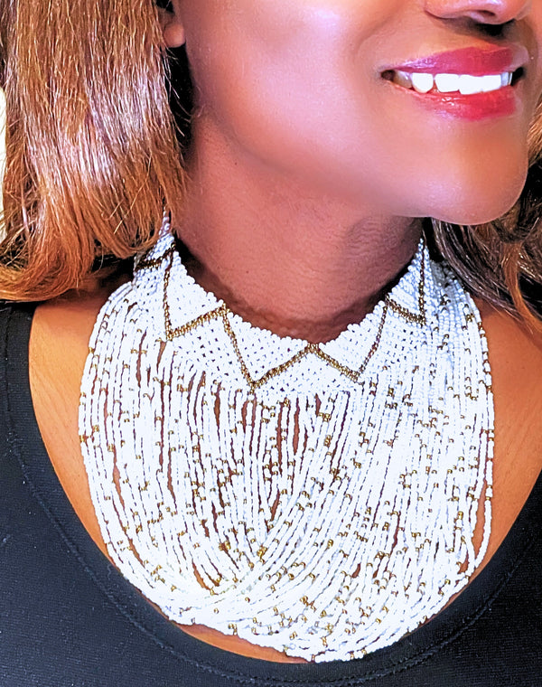 A close-up image of a person wearing a white beaded choker necklace with a geometric pattern and gold accents.